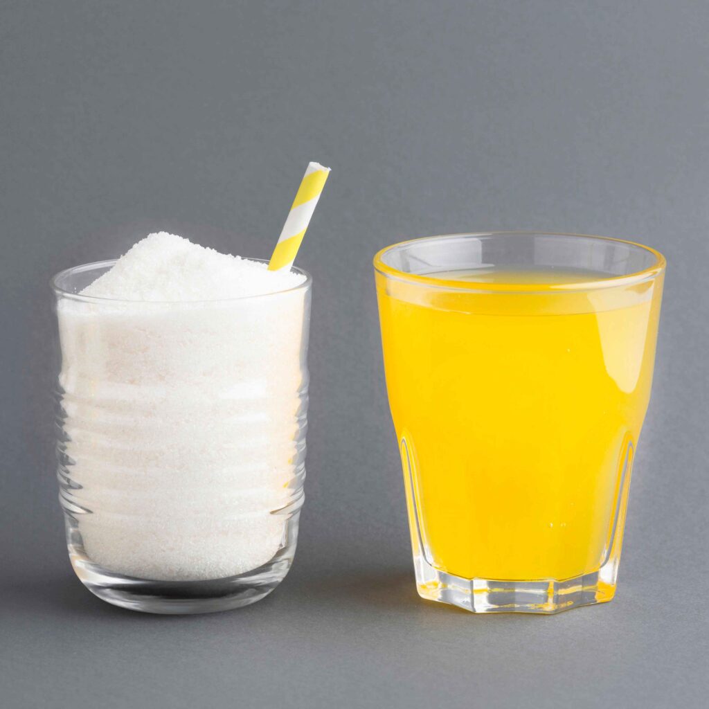 Um copo cheio de açúcar ao lado de um copo de suco 